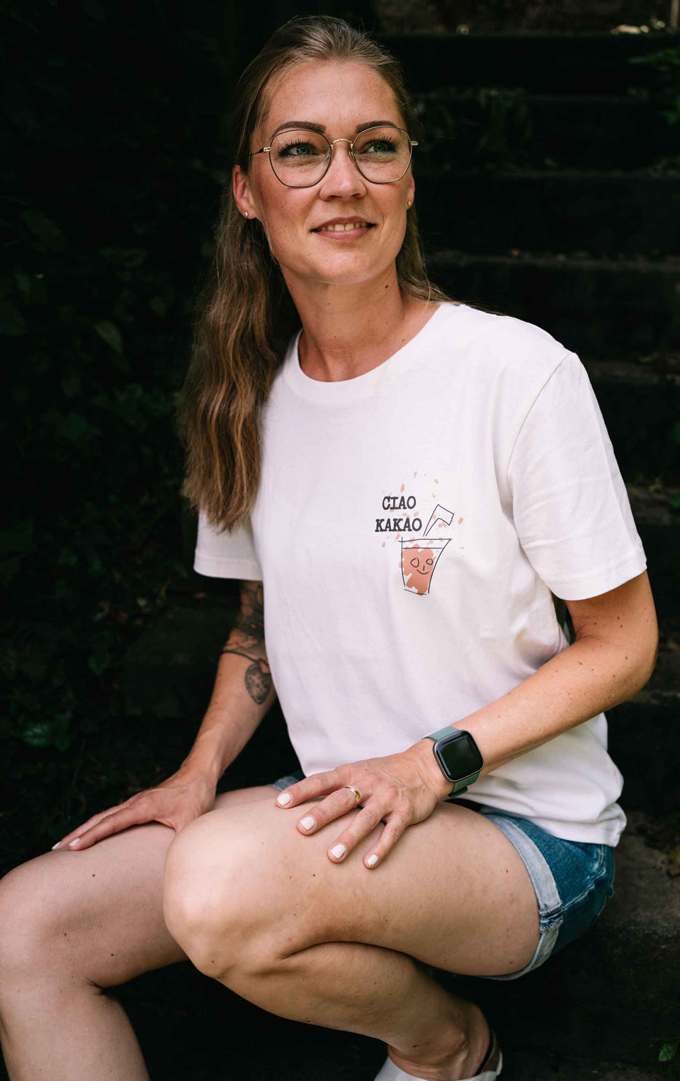 Ein Model trägt das Unisex-T-Shirt Ciao Kakao. Es ist Cremefarben aus recycelten Materialien und hat einen kleinen Druck auf der Brust.